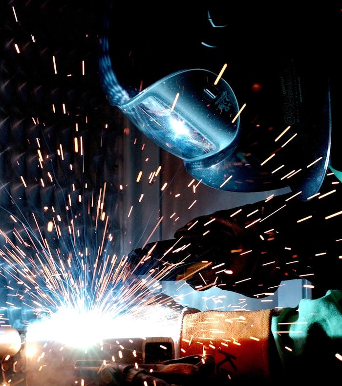Home A focused welder works with metal in an industrial setting, creating vibrant sparks.